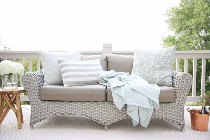 A wicker sofa on a white painted deck in an outdoor living room.