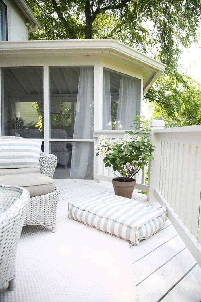 A white painted deck in an outdoor design with wicker furniture.