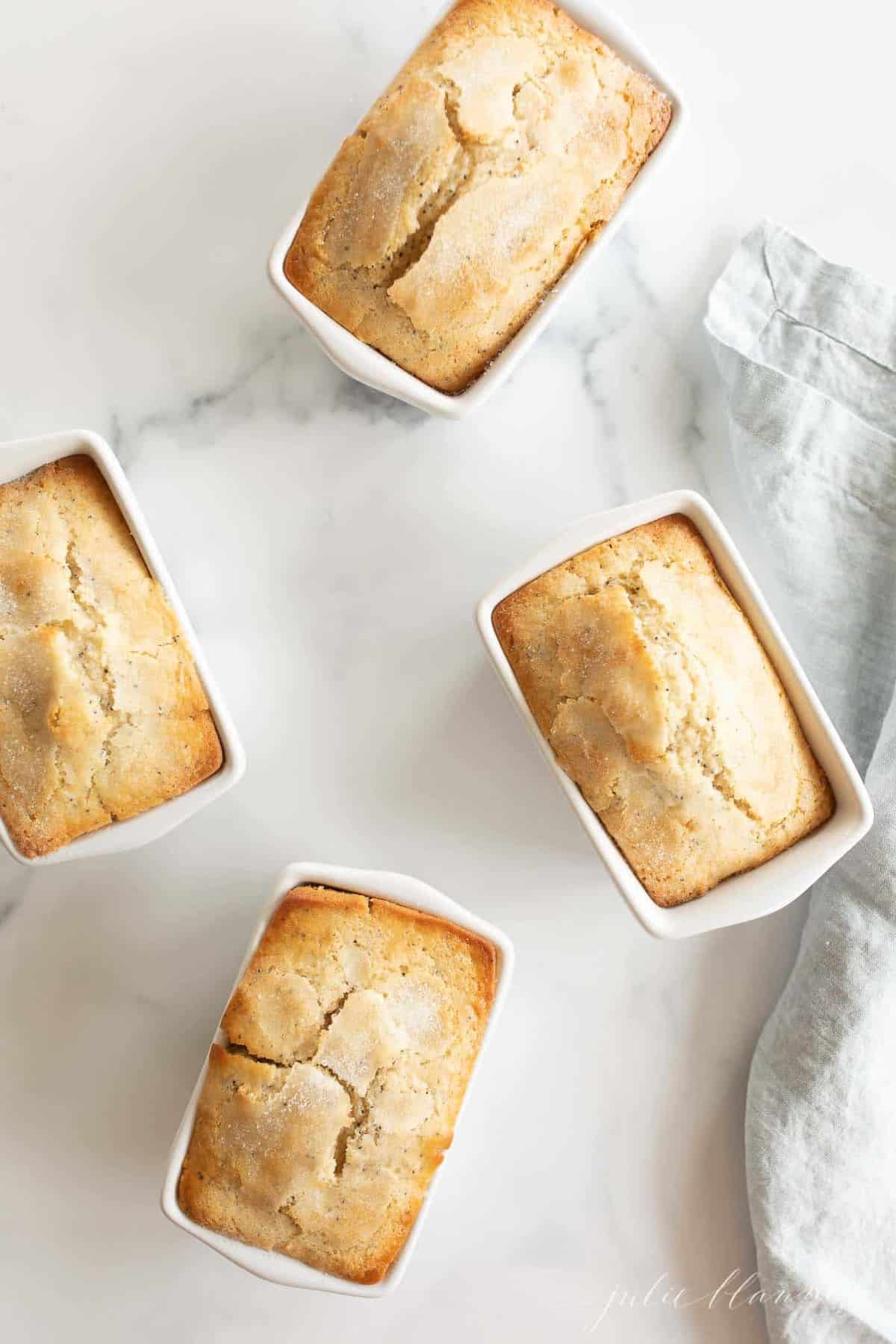 A poppy seed bread recipe made into several small white loaf pans on a marble surface.