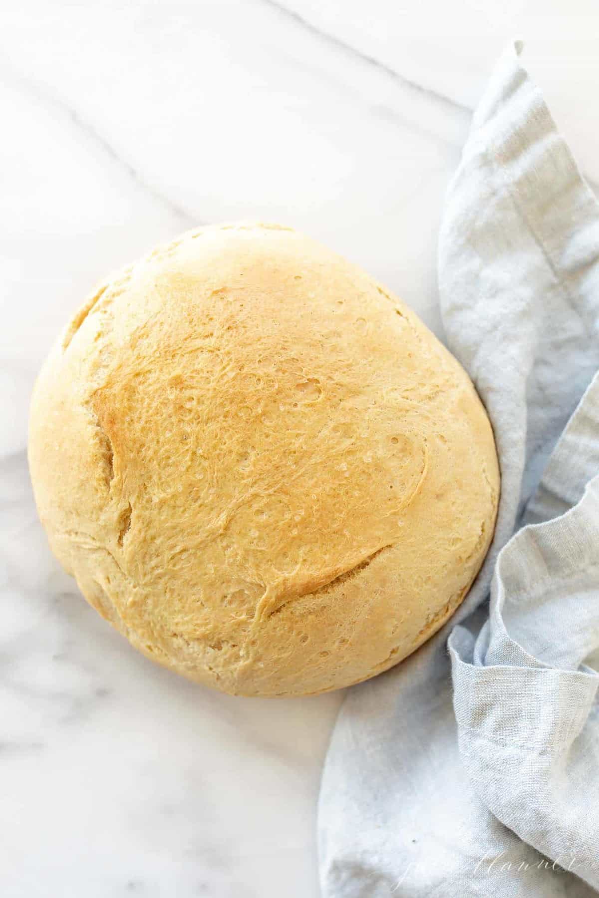 A round loaf of bread made with active dry yeast on a marble surface, blue linen napkin to the side.