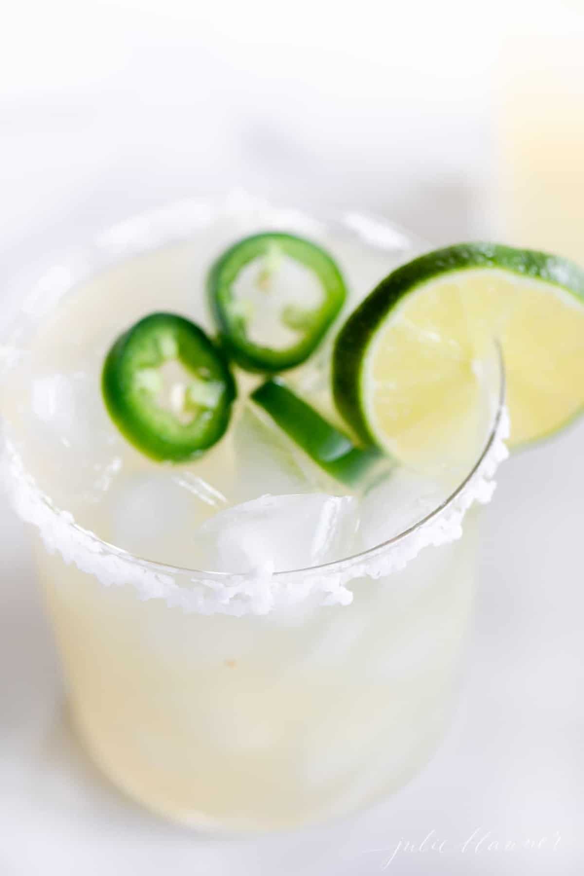 Jalapeño Margarita mix in a glass, with jalapeños and limes in the mixture.
