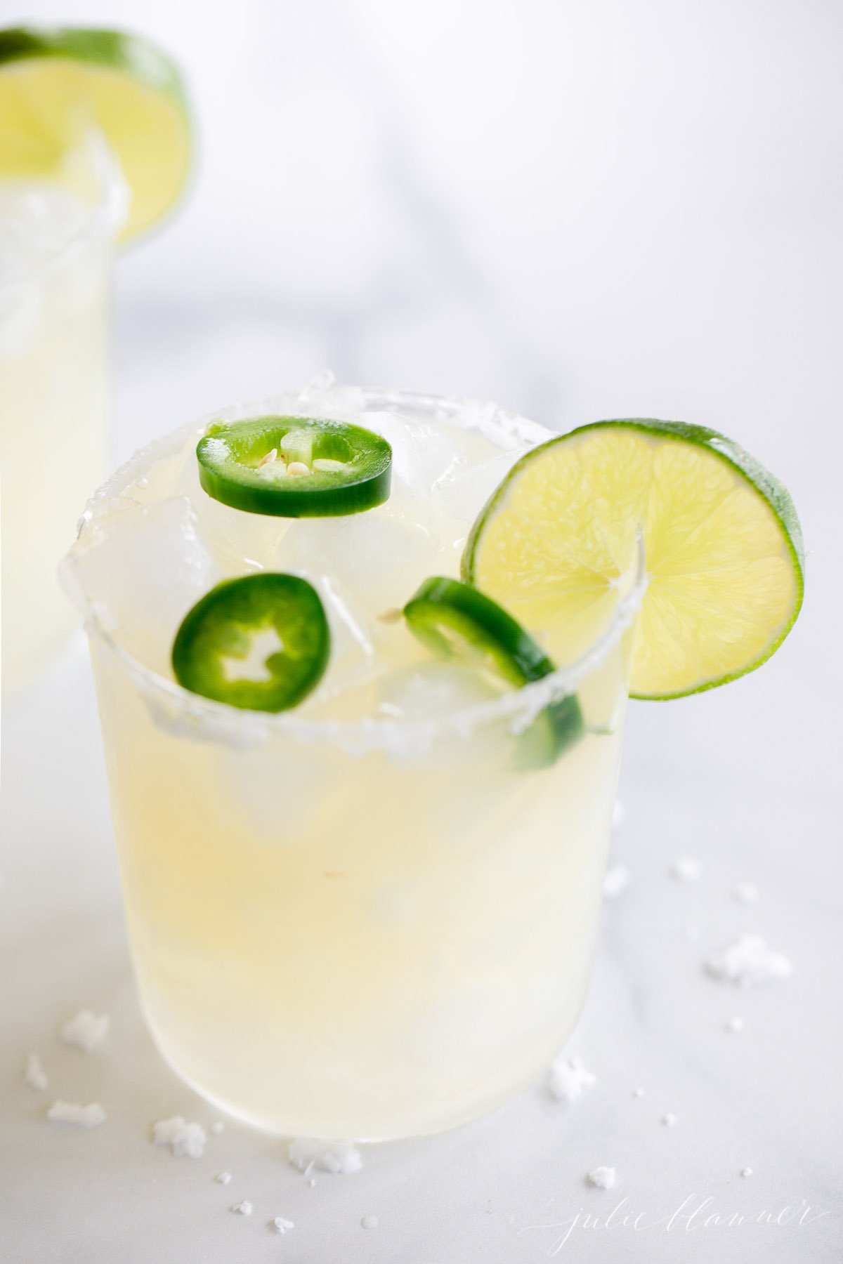 Two glasses of spicy jalapeno margarita with limes and jalapenos.
