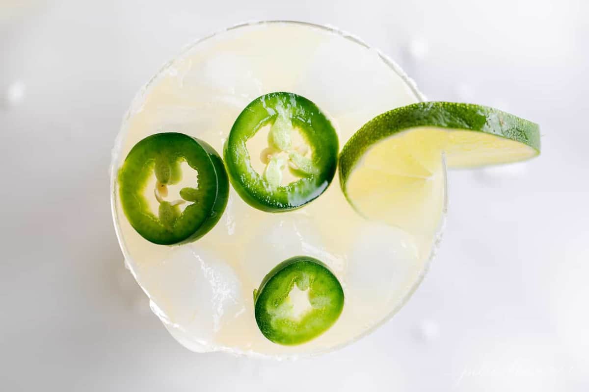 Jalapeño Margarita mix in a white pitcher, with jalapeños and limes in the mixture.