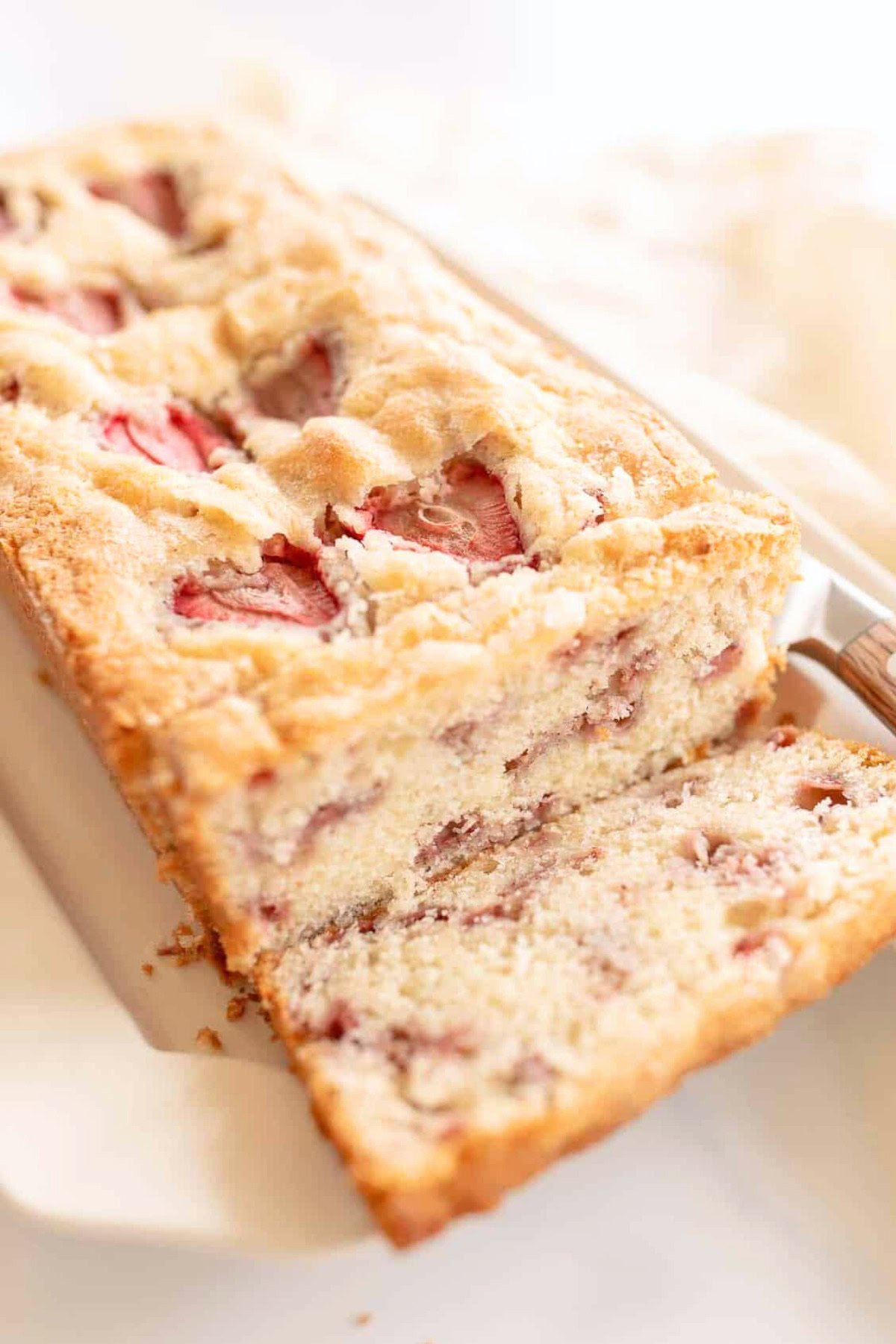 A close-up of a sliced loaf of strawberry bread, showcasing the moist interior with visible pieces of strawberries. The delectable strawberry bread is placed on a white surface, inviting you to try this delightful strawberry bread recipe.