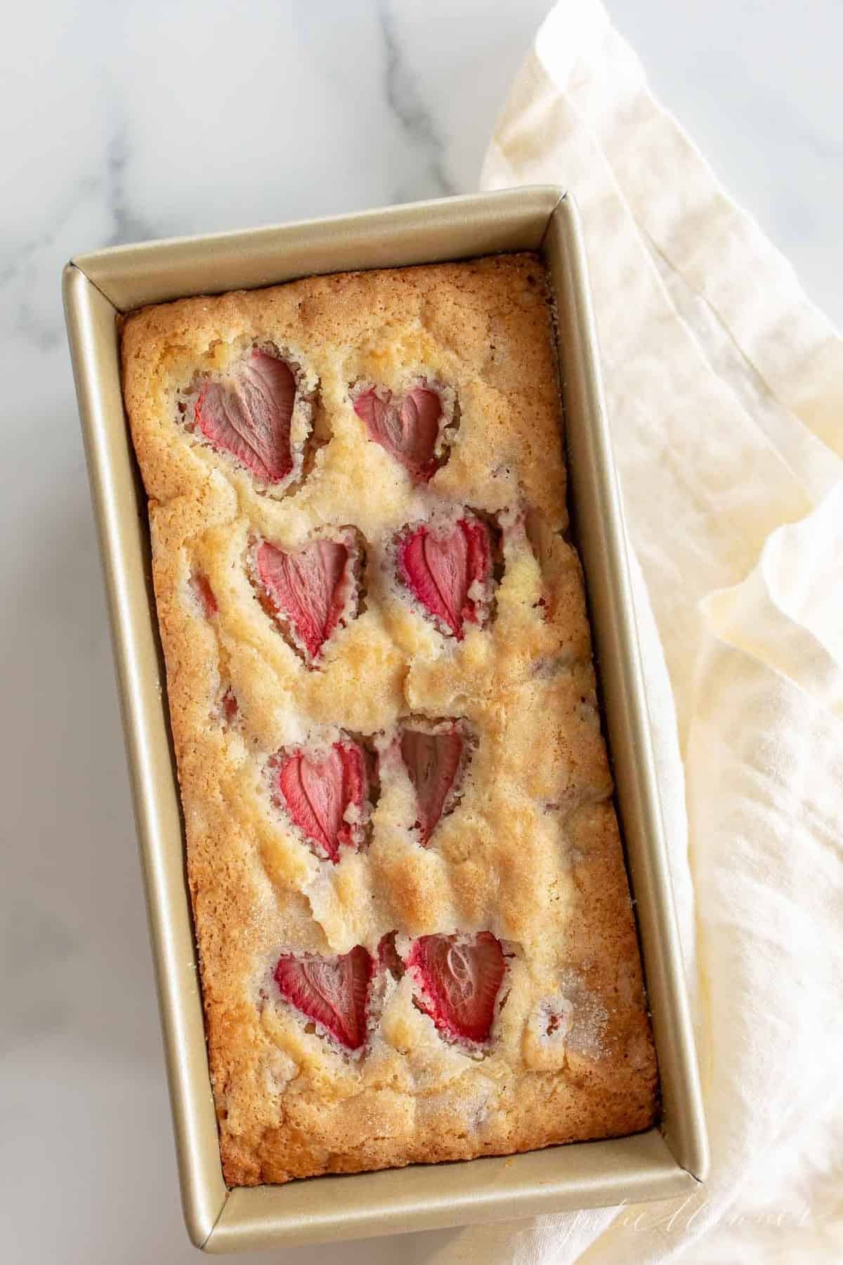 A marble background with a gold pan filled with fresh baked strawberry bread.