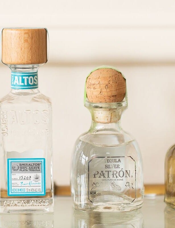 Four bottles of the best tequila for margaritas on a glass bar cart.
