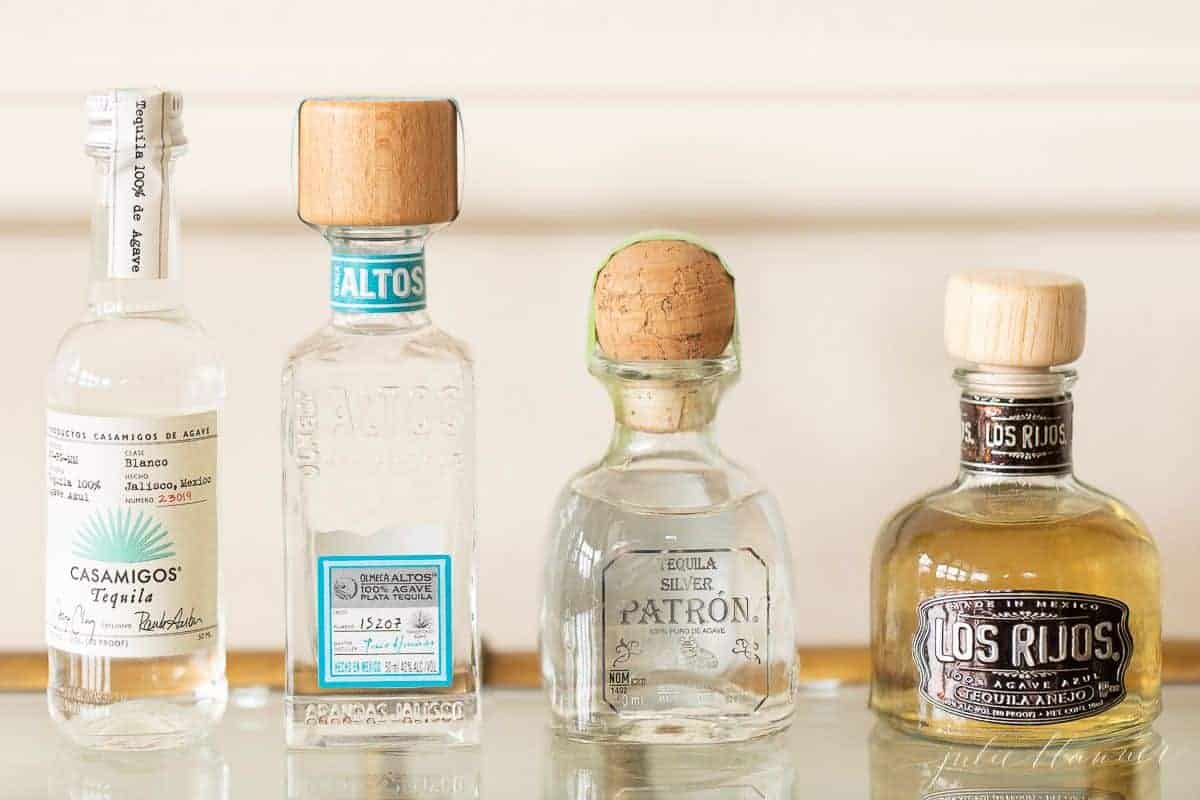 Four bottles of the best tequila for margaritas on a glass bar cart.