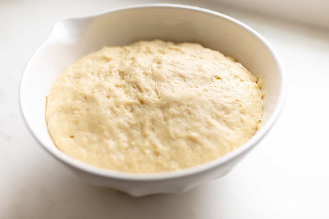 A white bowl filled with dough made with yeast.