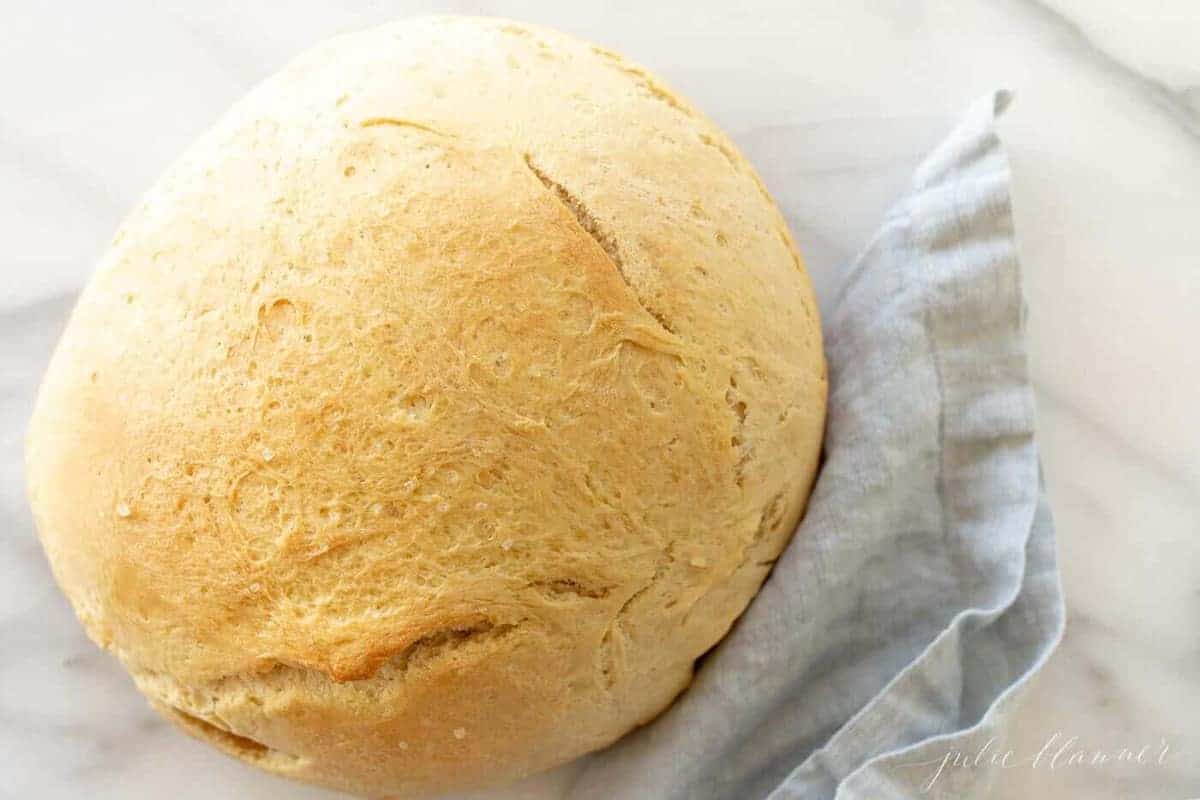 A round loaf of bread made with instant yeast on a marble surface, blue linen napkin to the side.