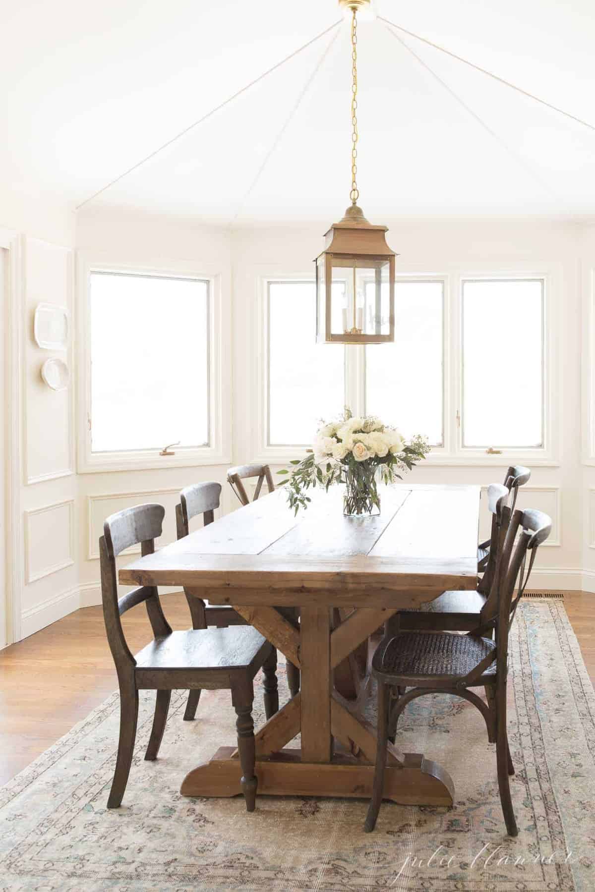 A white dining room with a farm table and a vintage kilim style Turkish rug.