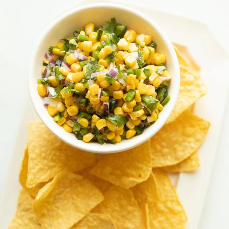 A white bowl full of chipotle corn salsa, surrounded by tortilla chips.
