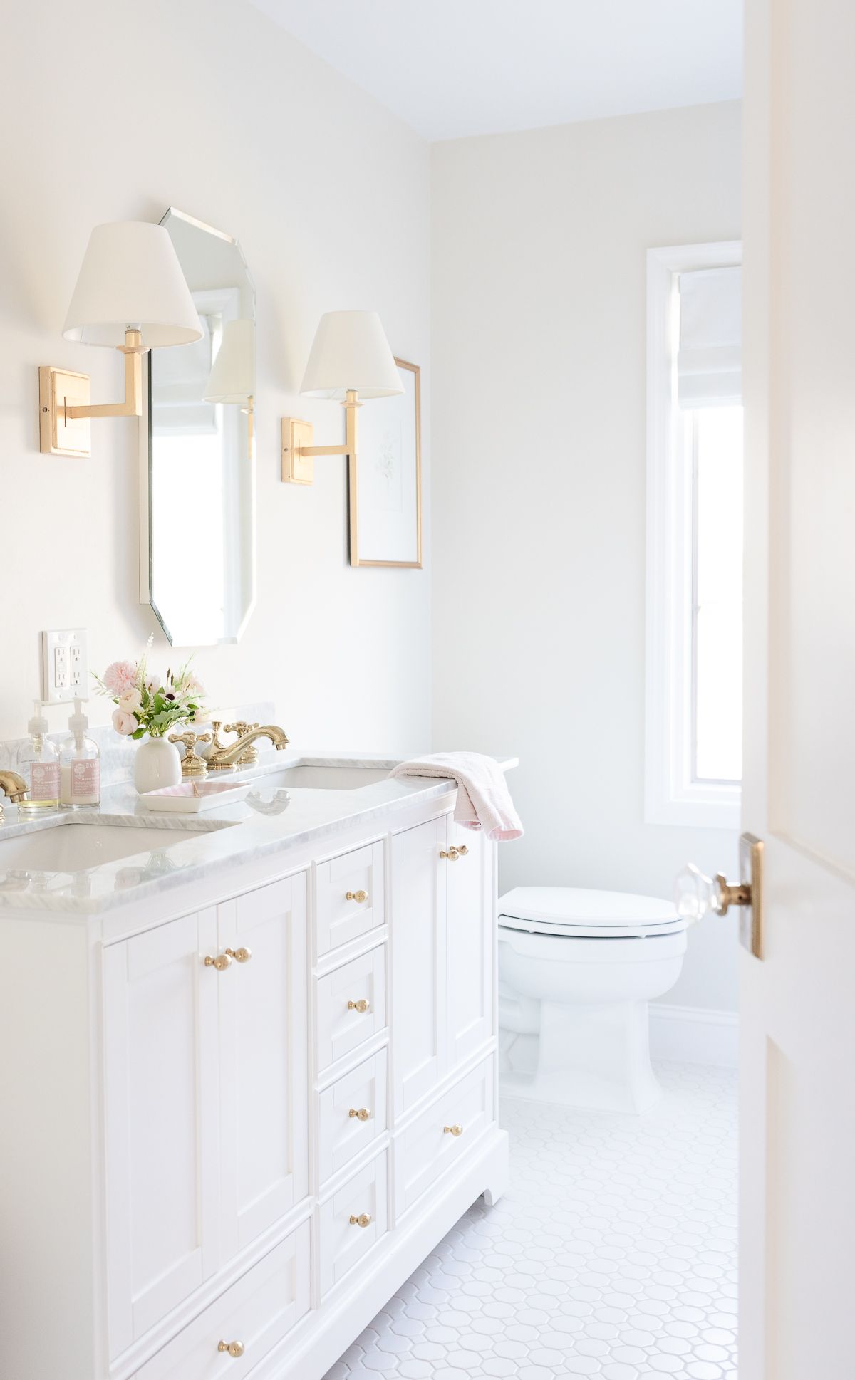 A white and bright bathroom with a window and two sconces