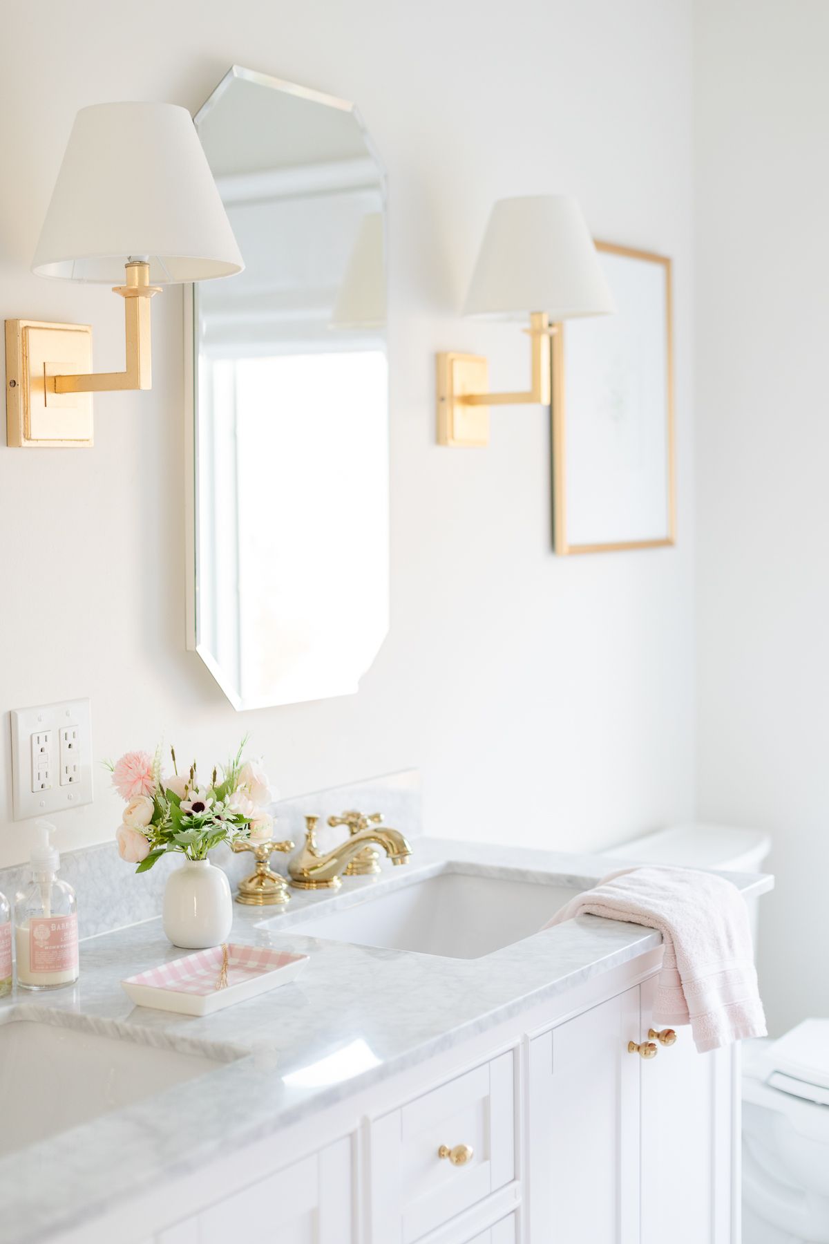 A white bathroom with two mirrors and two gold sconces