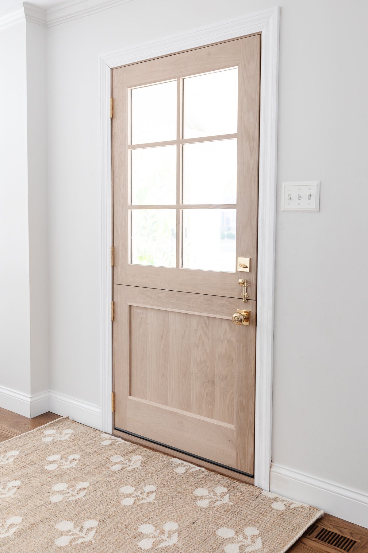 A soft wood dutch door in a white entryway, open to the outdoors