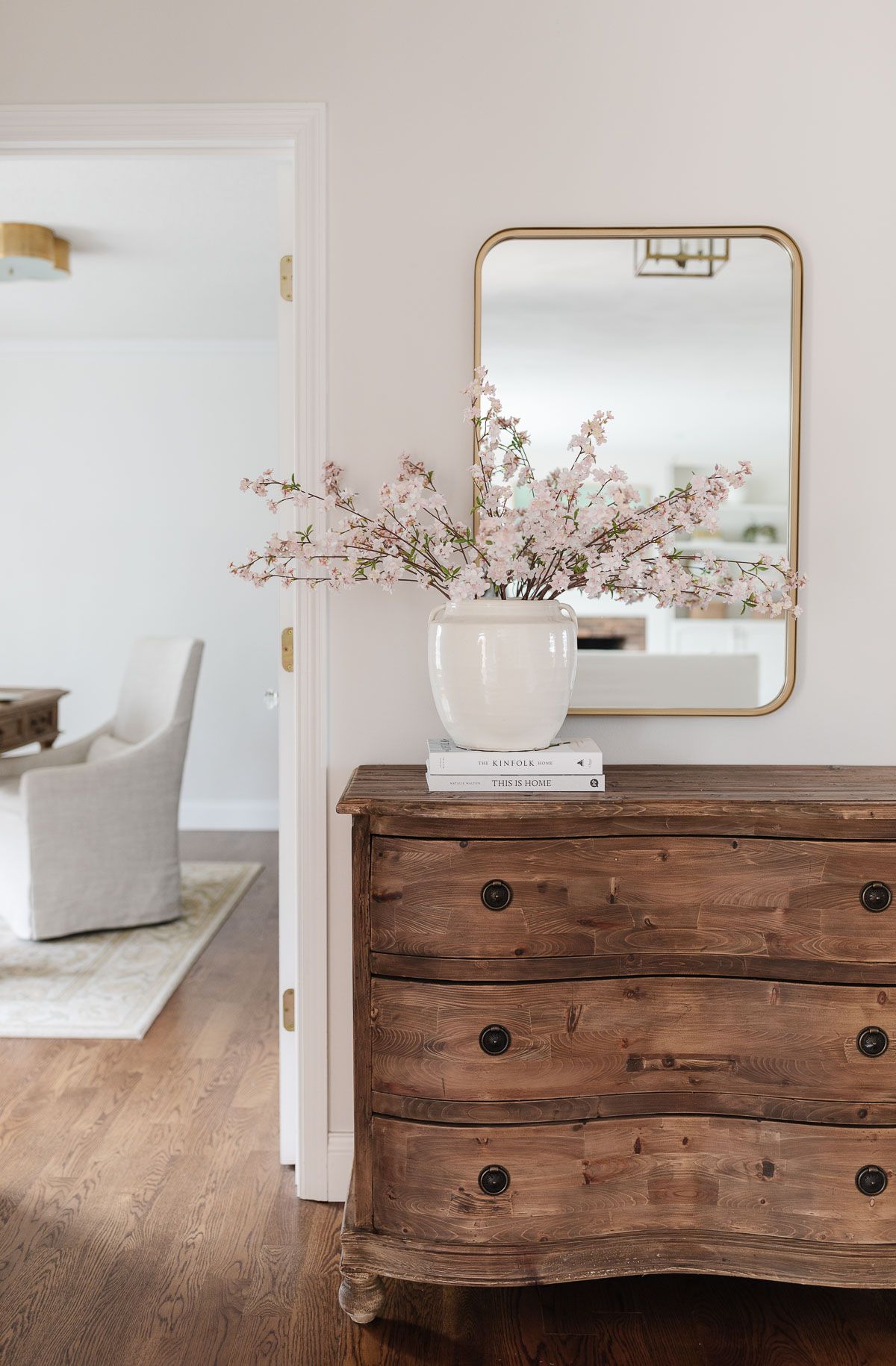 An entryway with a wooden chest and a brass mirror hanging above