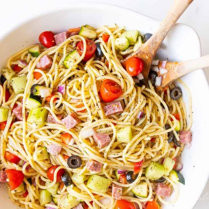 A white bowl with spaghetti salad, wooden spoons to the side.