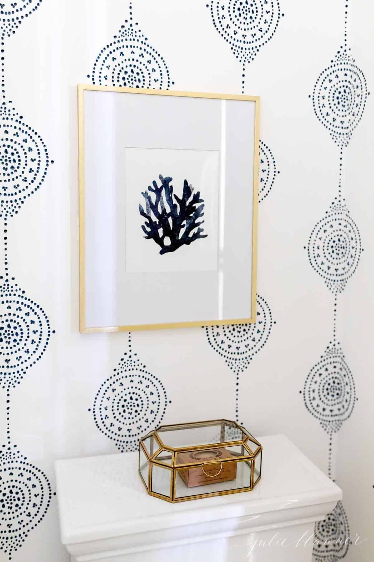 Blue and white patterned bathroom wallpaper with seashell art over the toilet.