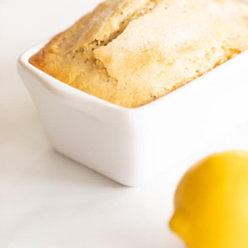 A marble counter top background with a small loaf of lemon poppy seed bread recipe, lemon to the side.