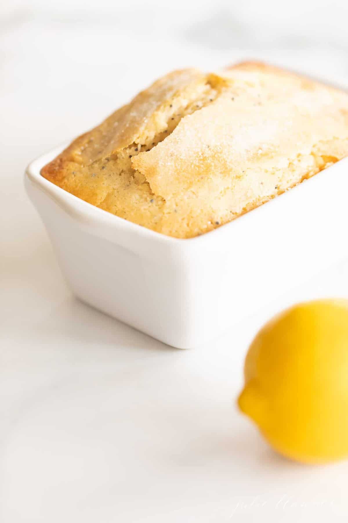 A marble counter top background with a small loaf of lemon poppy seed bread recipe, lemon to the side.