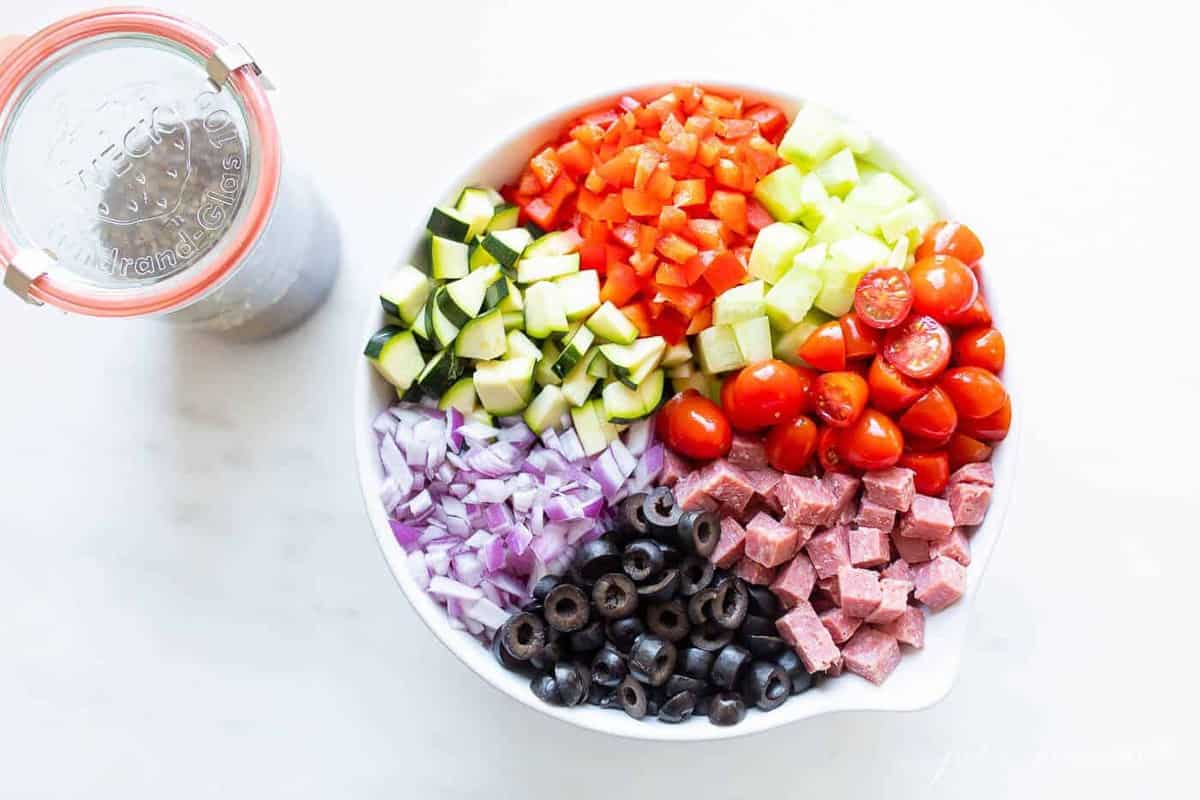 A white bowl filled with ingredients for a homemade spaghetti salad recipe.