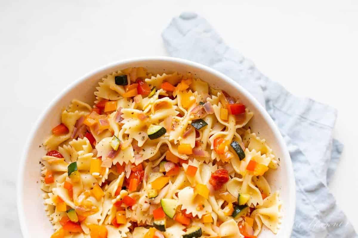 A white bowl filled with a fresh vegetarian pasta salad.