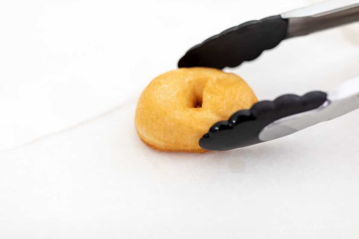 A doughnut being picked up with tongs. 
