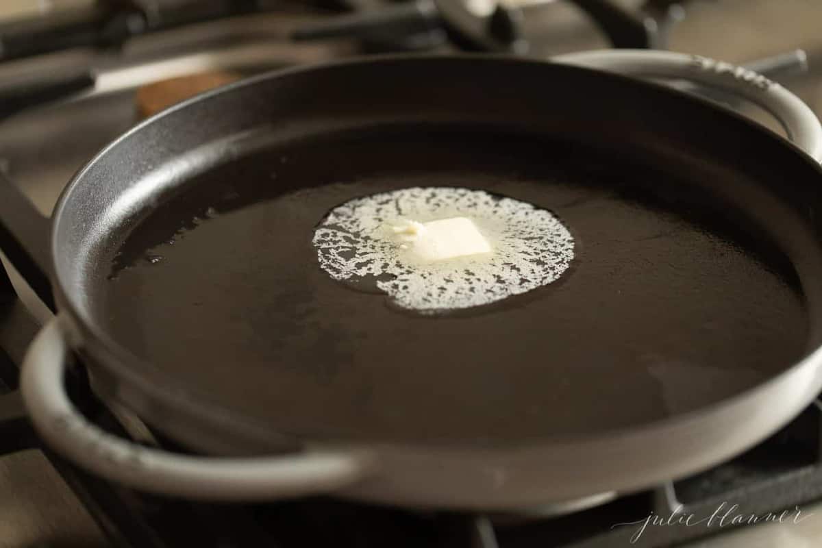 A cast iron burger pan with a pat of butter starting to melt.