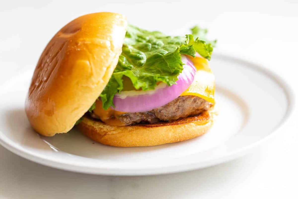 A close up shot of a cast iron burger stacked with lettuce, red onions and cheese.