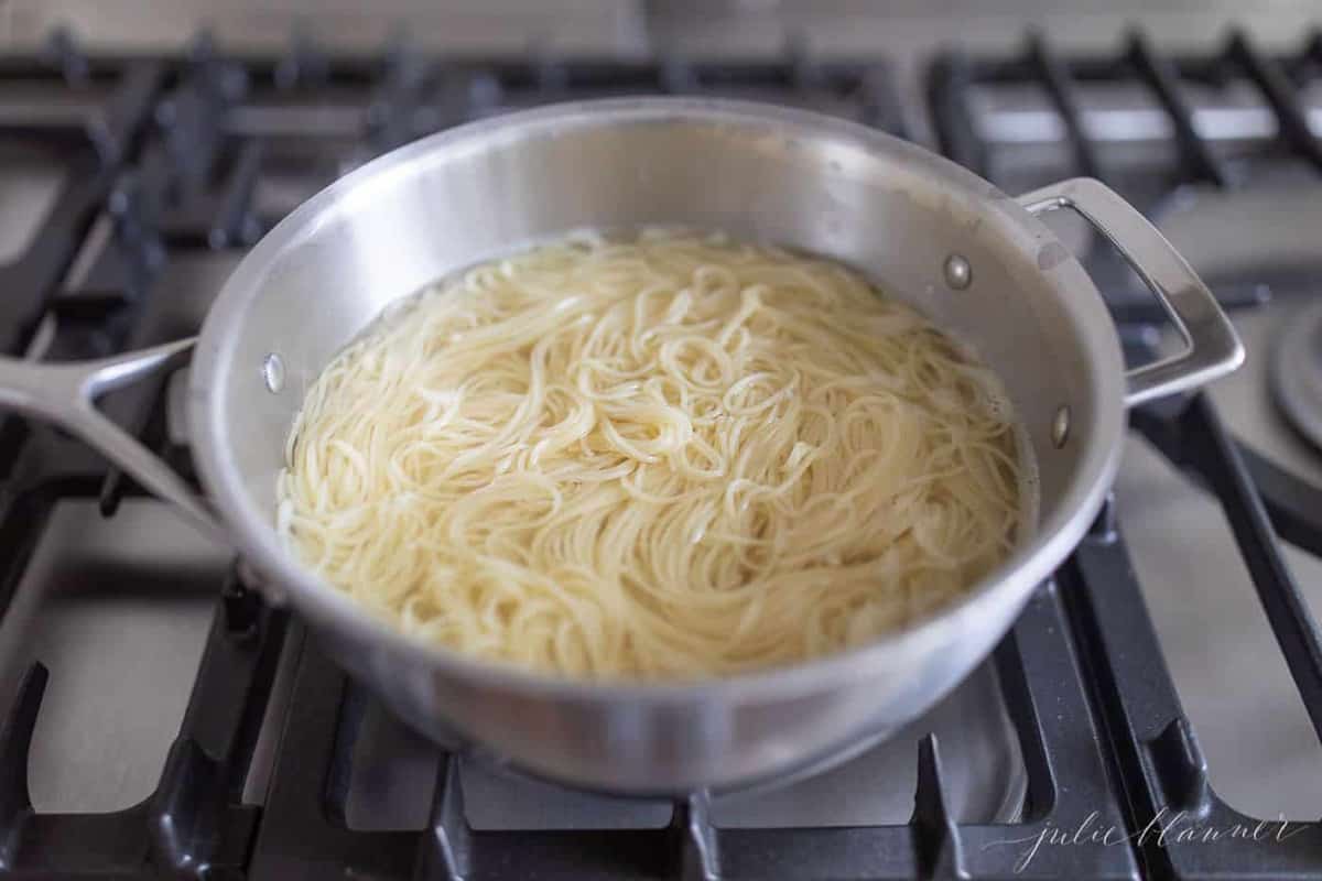 A silver pot of boiling water with spaghetti noodles inside.