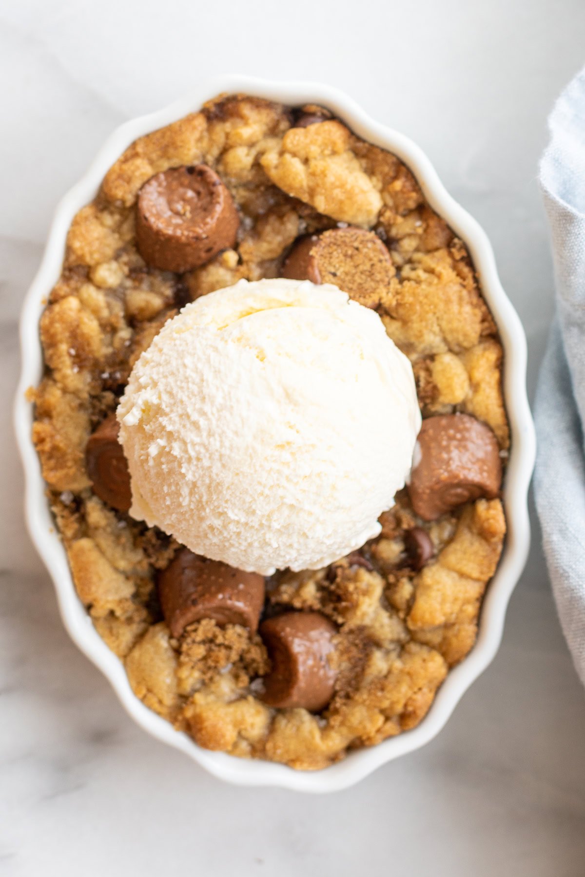An oval bowl filled with a crumbly chocolate chip cobbler topped with a scoop of vanilla ice cream and small chocolate pieces.