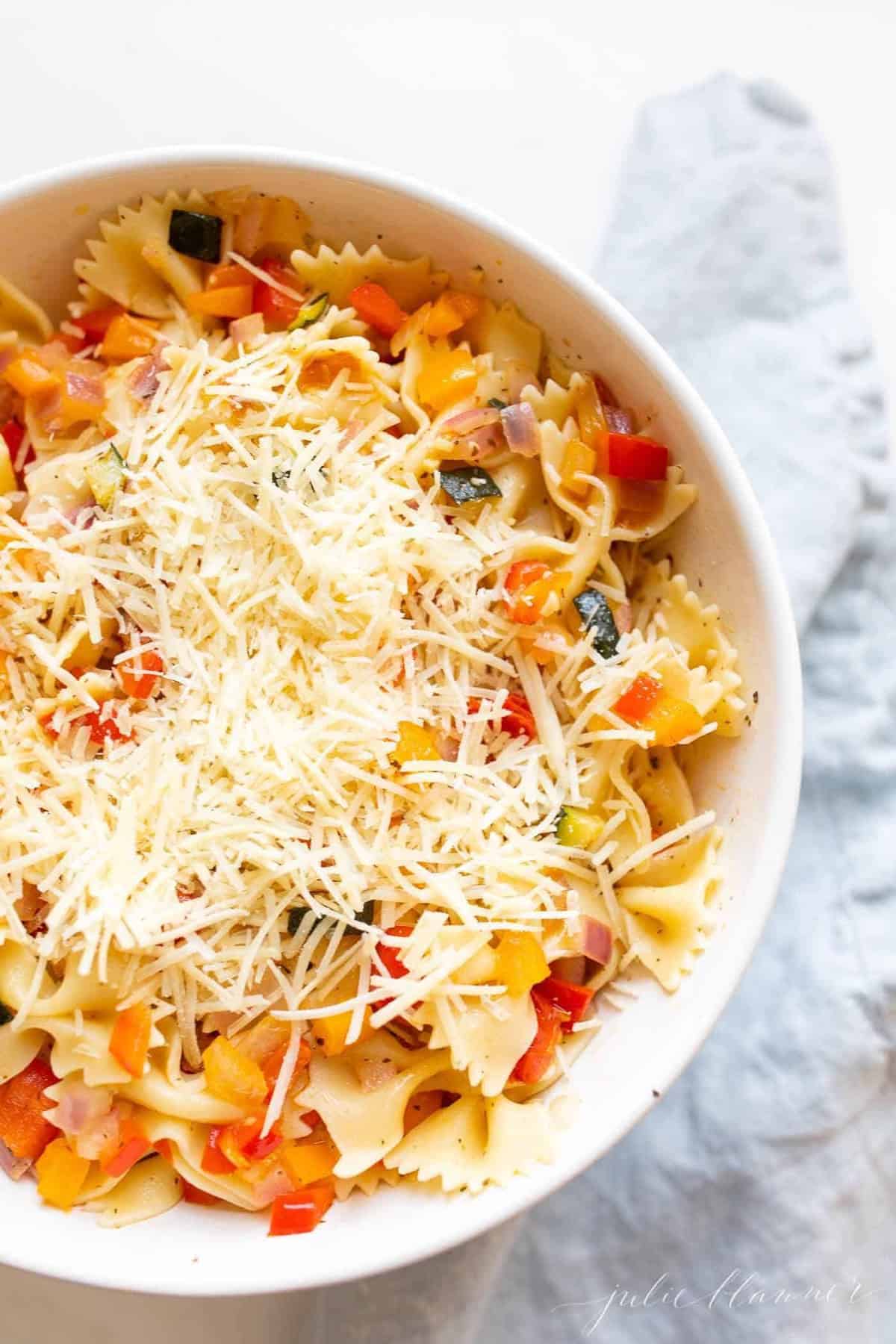 A white bowl filled with a fresh vegetarian pasta salad topped with Parmesan cheese.