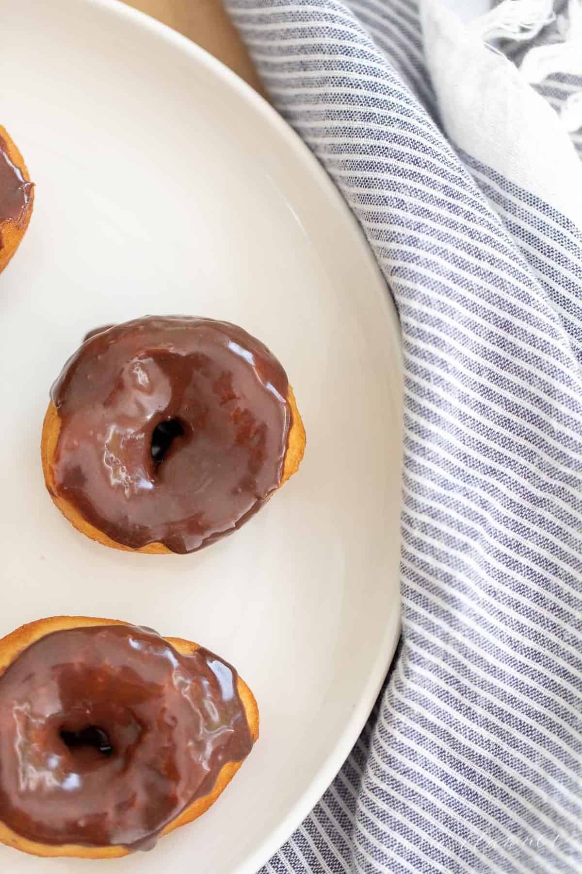 Biscuit donuts covered in chocolate icing on a white plate.