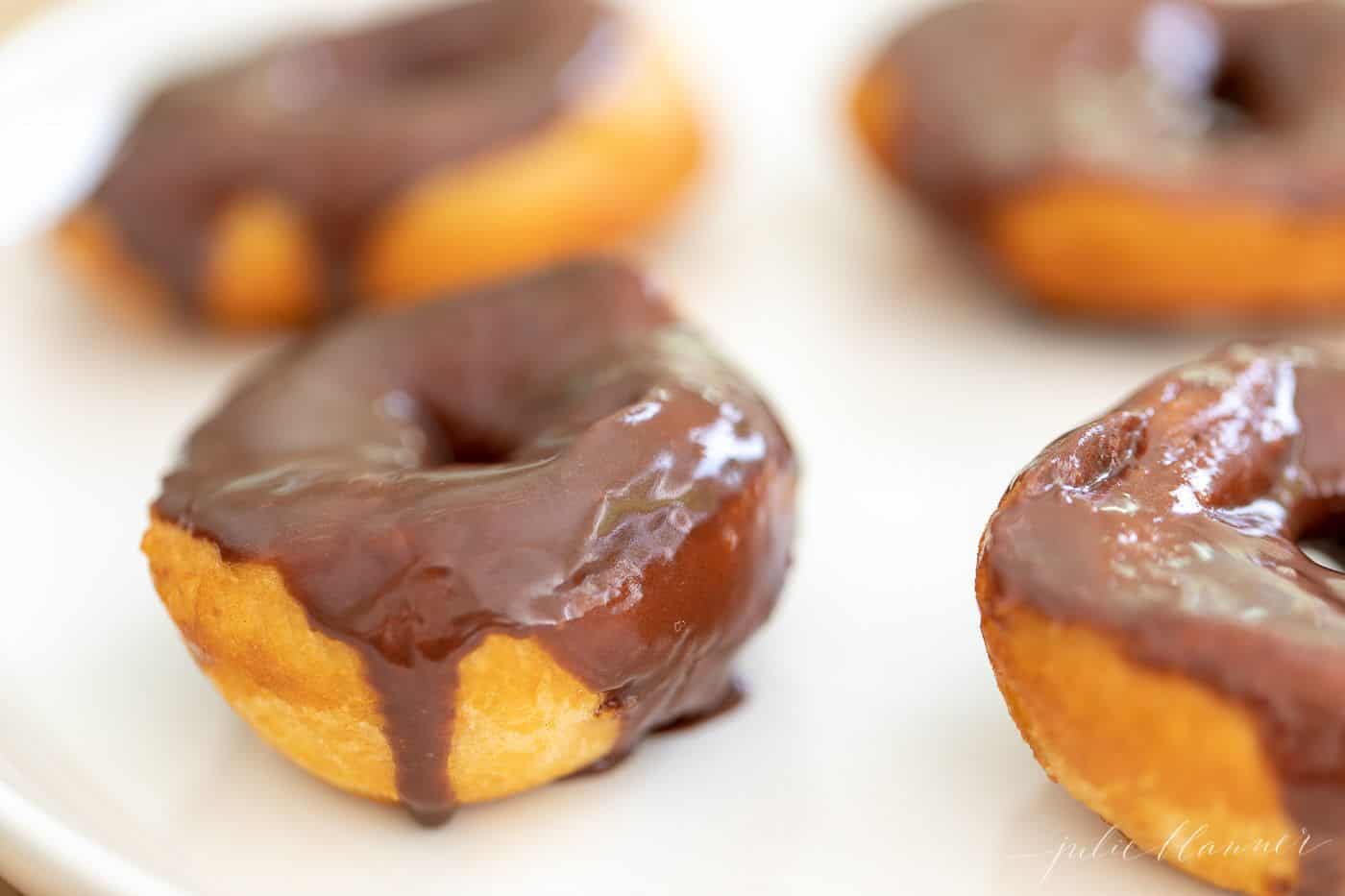 Biscuit donuts covered in chocolate icing on a white plate.