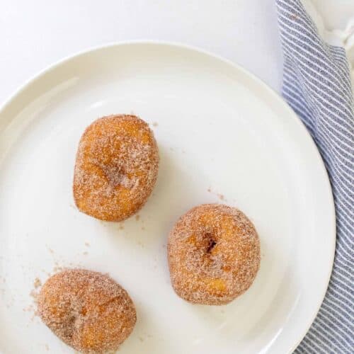 Um prato branco com três rosquinhas de biscoito cobertas com açúcar de canela.