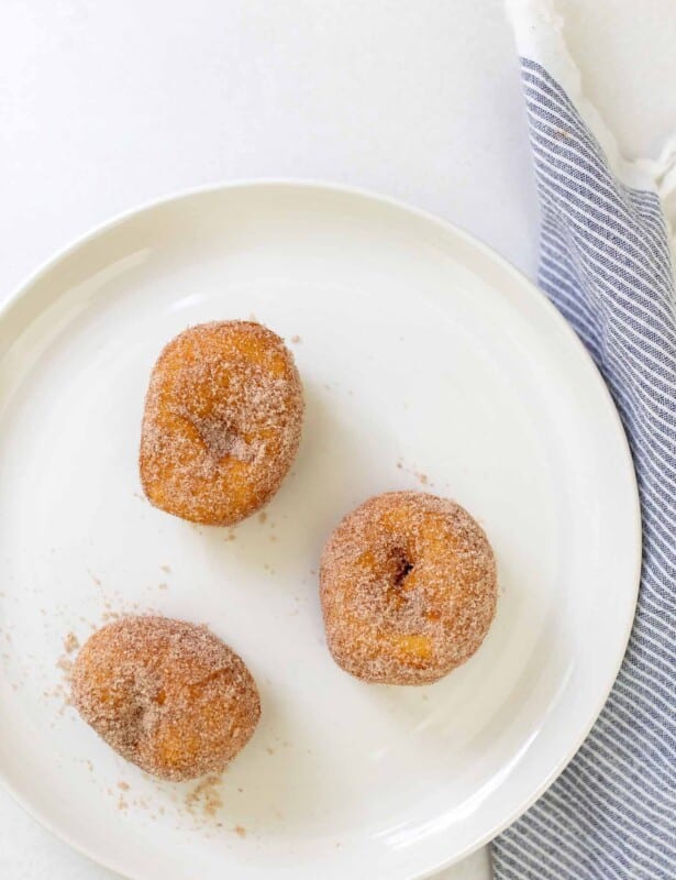 A white plate with three biscuit donuts covered in cinnamon sugar.