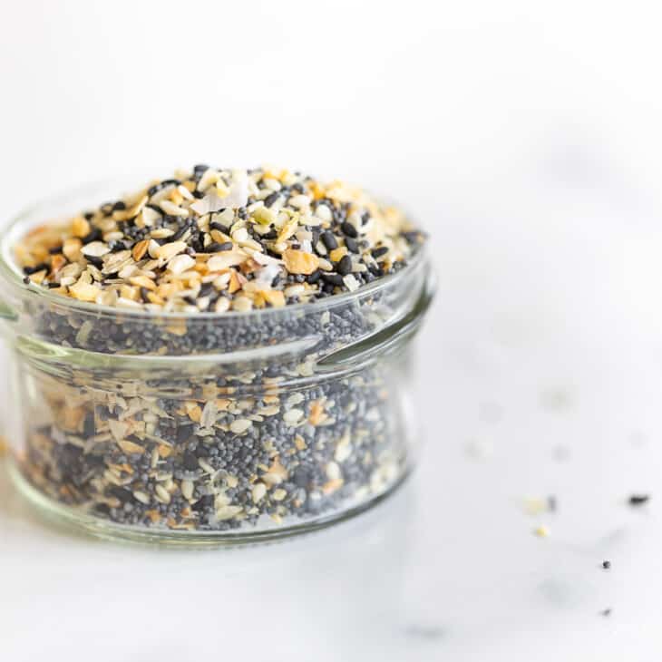 A clear glass jar on a marble surface, filled with everything bagel seasoning.