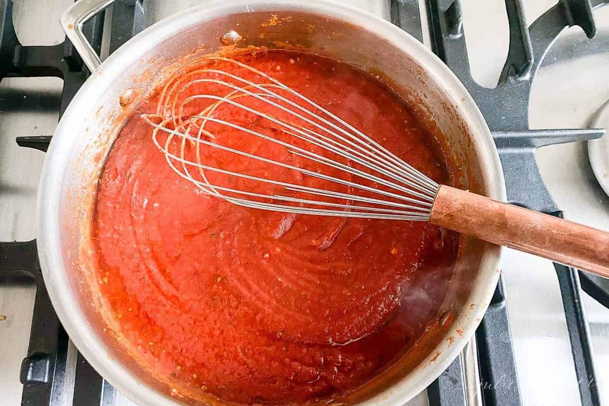 A silver sauce pan filled with homemade pizza sauce recipe on cooktop.