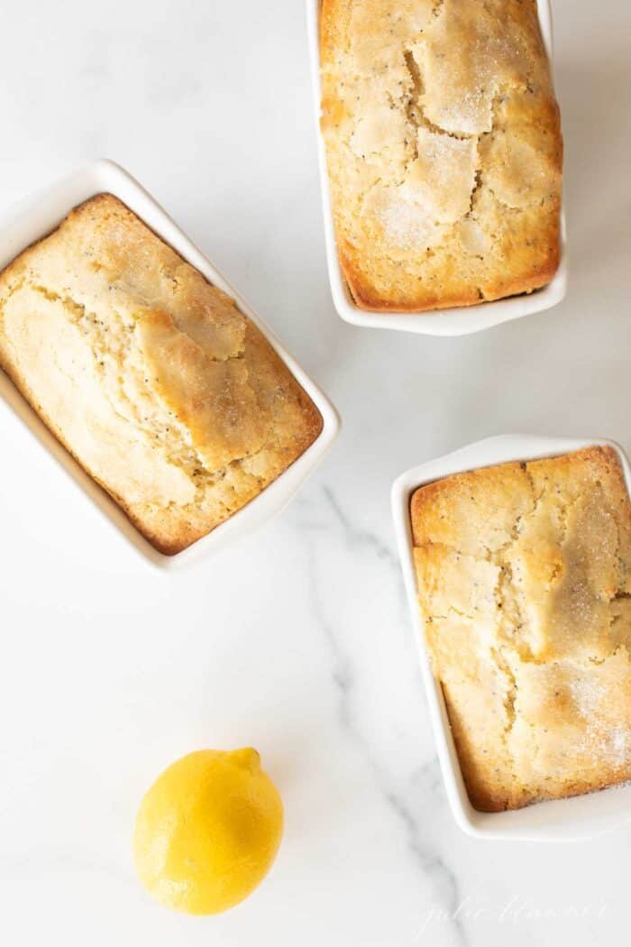 A marble surface with three small loaves of lemon poppy seed bread.