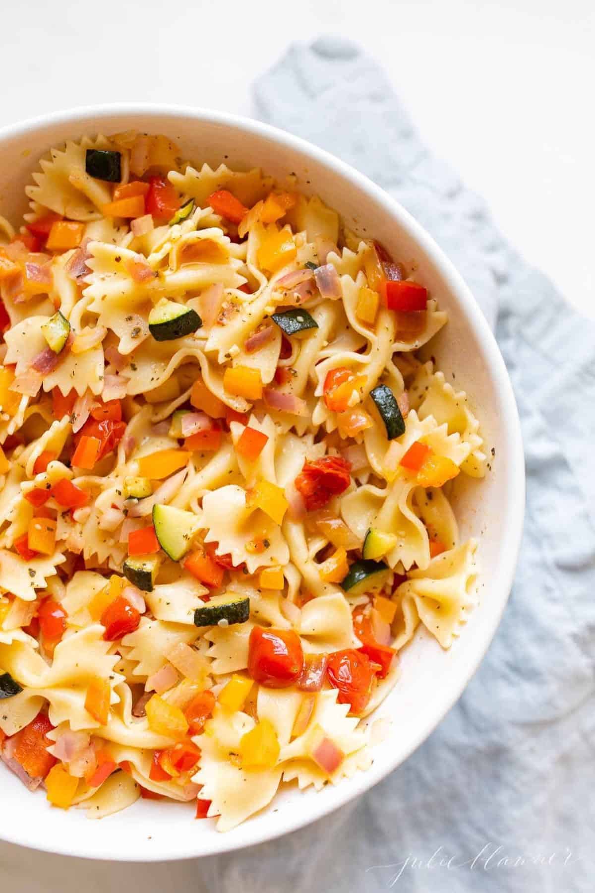 A white bowl filled with a fresh vegetarian pasta salad.