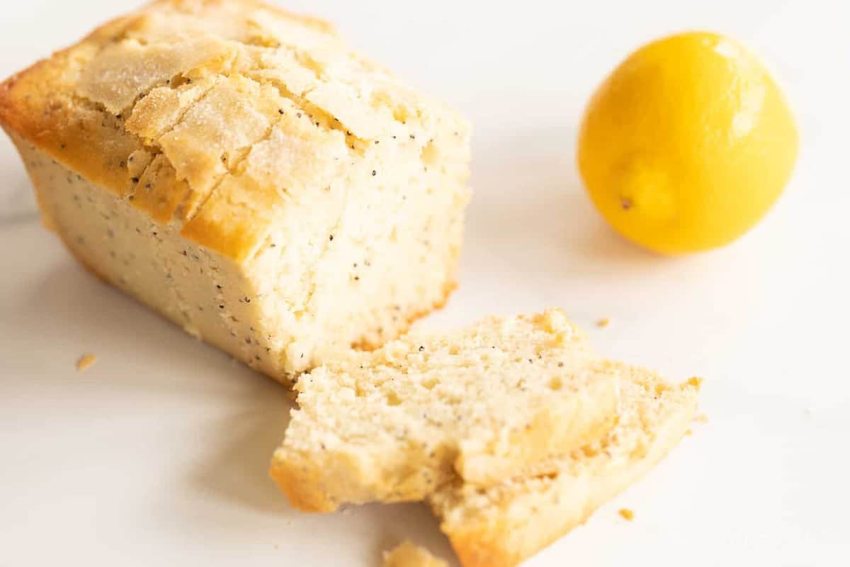 A marble counter top background with a small loaf of lemon poppy seed bread recipe, lemon to the side.
