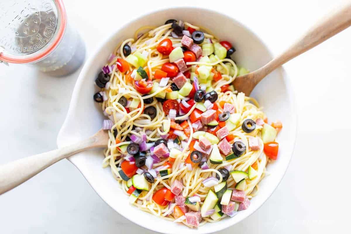 A white bowl with spaghetti salad, wooden spoons to the side.