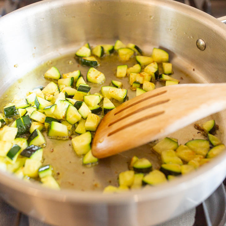 Vegetables cooking in a stainless steel pan on a stovetop.