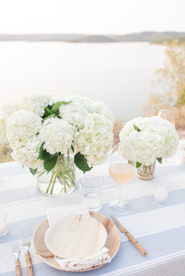 Elegant outdoor dining setup featuring lush hydrangea centerpieces on a table overlooking a serene lake.