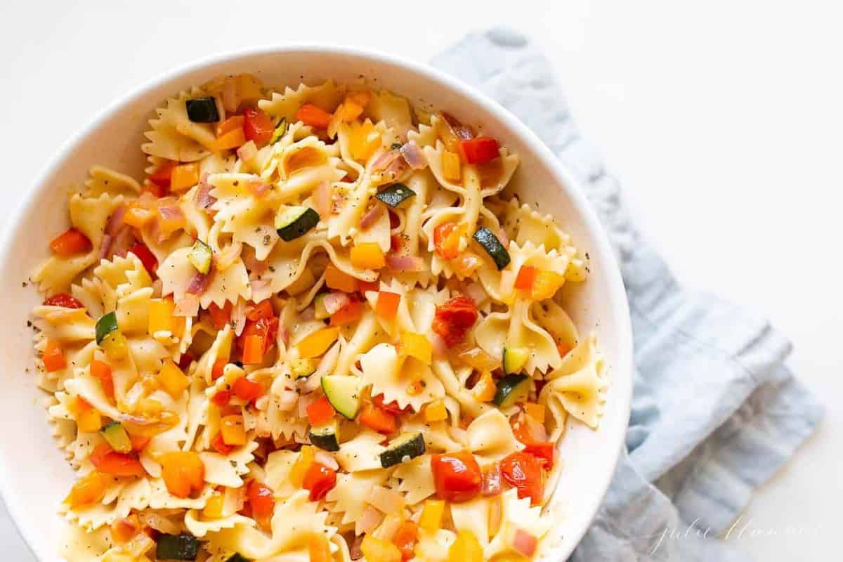 A white bowl filled with a fresh vegetarian pasta salad.