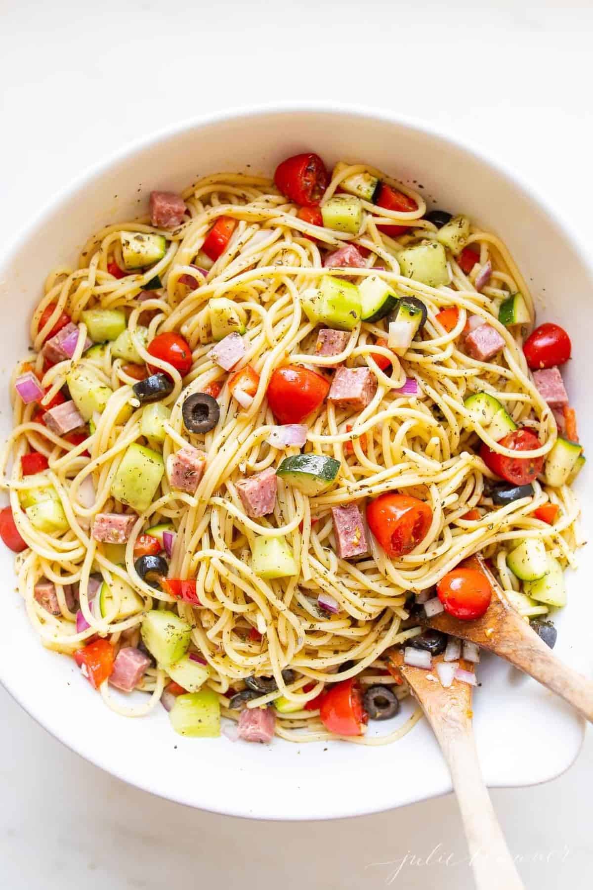 A white bowl with spaghetti salad, wooden spoons to the side.