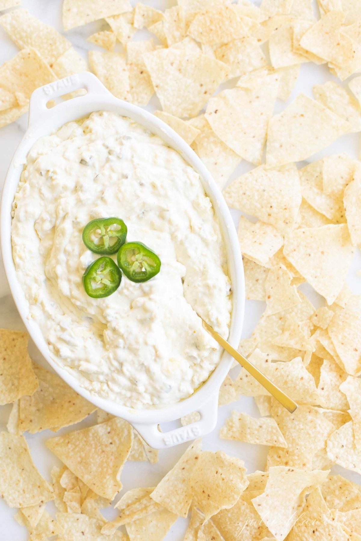 An oval serving dish full of jalapeno dip, surrounded by tortilla chips.