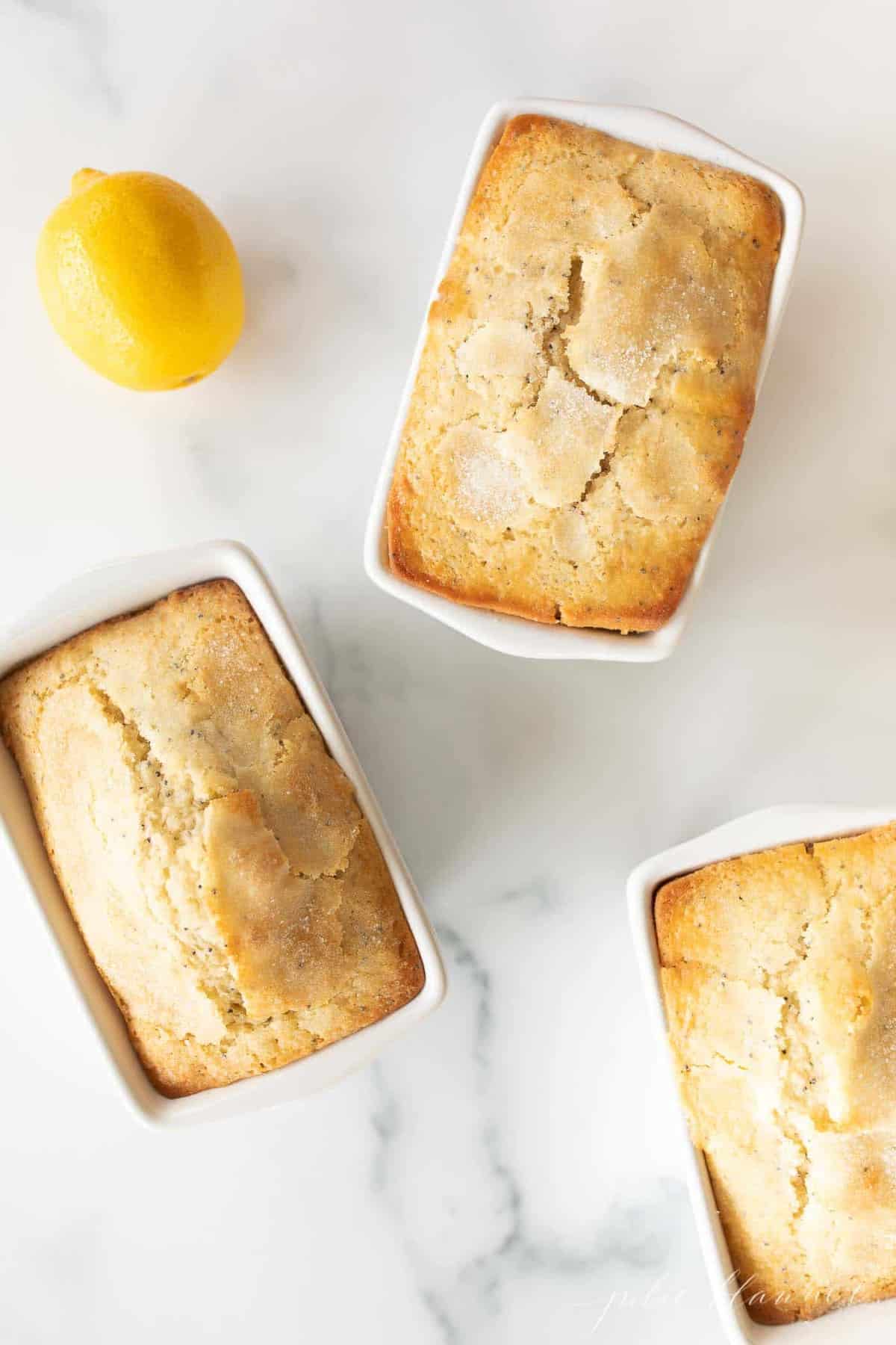 A marble surface with three small loaves of lemon poppy seed bread.