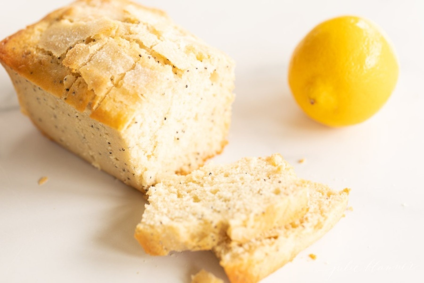 A loaf of lemon poppy seed bread, sliced, with a lemon beside it.