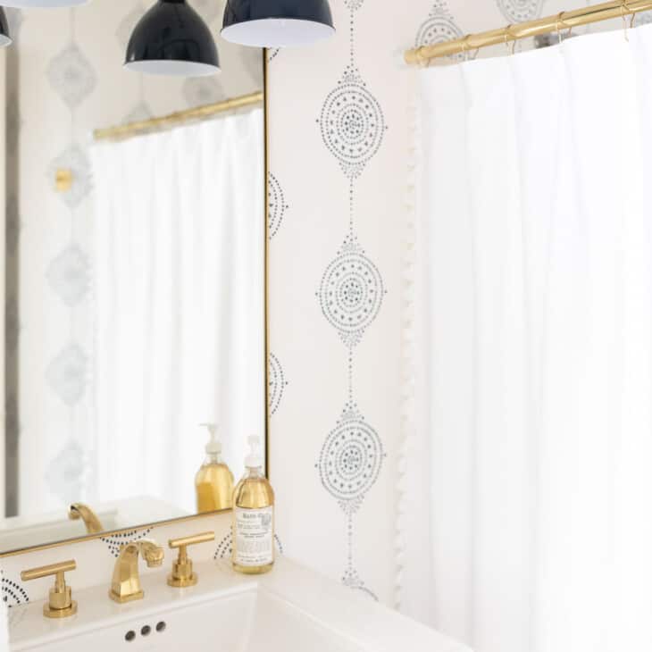 A modern bathroom with a navy light fixture and navy and white patterned bathroom wallpaper.