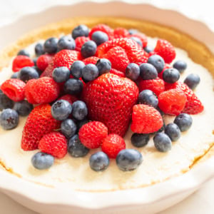 A no bake lemon pie cheesecake topped with fresh strawberries, blueberries, and raspberries in a white ceramic dish.